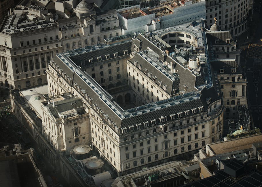 An aerial view of a large historic building located in Aldwych, London, with a central courtyard and multiple floors featuring rows of windows and decorative stonework. Surrounding structures include other multi-storey buildings with classical architectural details. The city streets around the building are visible, with cars and pedestrians, and construction work can be seen in the background. The scene captures the urban environment where site access for house removals and furniture transport may be considered during a home relocation, with the building's layout indicating potential loading points for moving services provided by Man with Van Aldwych, specialists in removals and packing and moving logistics.