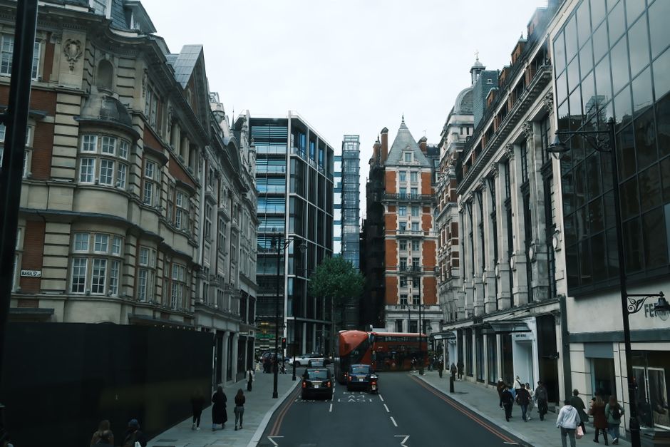 A street scene showcasing a large, multi-storey residential building with a curved facade and ornate architectural details in a warm yellow tone, situated on a corner of a city street. To the right, t